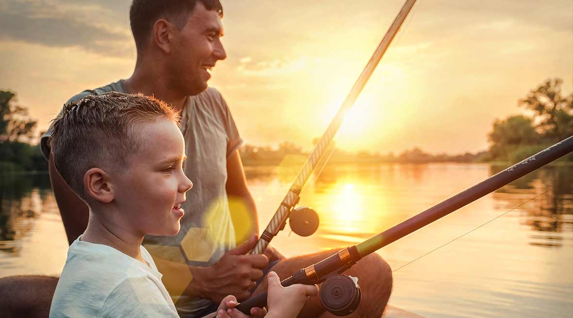 Man and child holding fishing rods on a boat with sunset and lake behind them